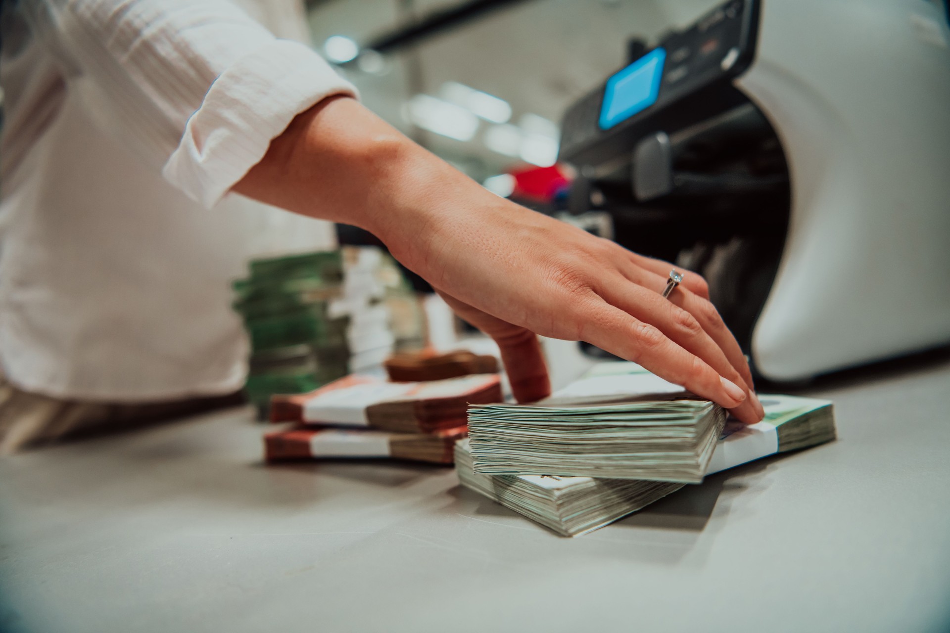 Bank employees using money counting machine while sorting and counting paper banknotes inside bank vault. Large amounts of money in the bank